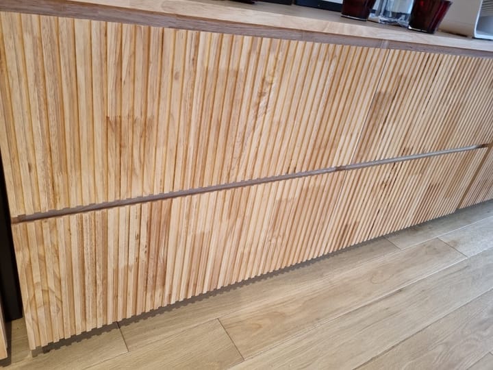 Close-up of a custom solid-wood cabinet with a fluted front and integrated drawer pull